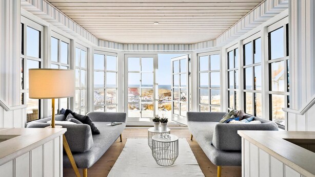 A spacious room with large windows, a grey sofa, a small round coffee table, and a lamp. - Lovely home in Hjørring with sauna (Hjørring)