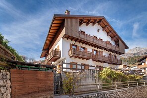 Un chalet a più piani con balconi in legno, pareti in pietra e montagne sullo sfondo.