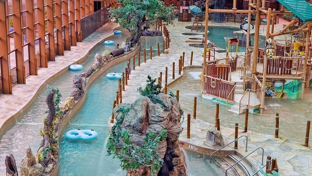 Een overdeeld watergebied met meerdere zwembaden, houten speelconstructies en een rotsachtig eiland met een beerbeeld.