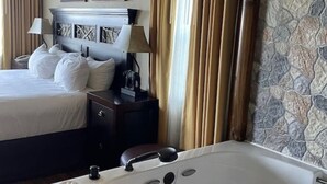 Hotelkamer met een groot bed, een apart zithoekje met een fauteuil, een badkuip en twee schilderijen aan de muur.
