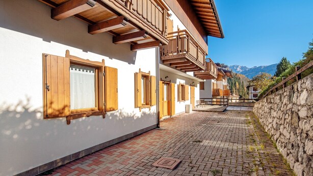 Un edificio con balcones de madera, un camino de ladrillo y un muro de piedra.