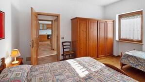 Un dormitorio con cama, armario de madera, una silla y ventana con cortinas.