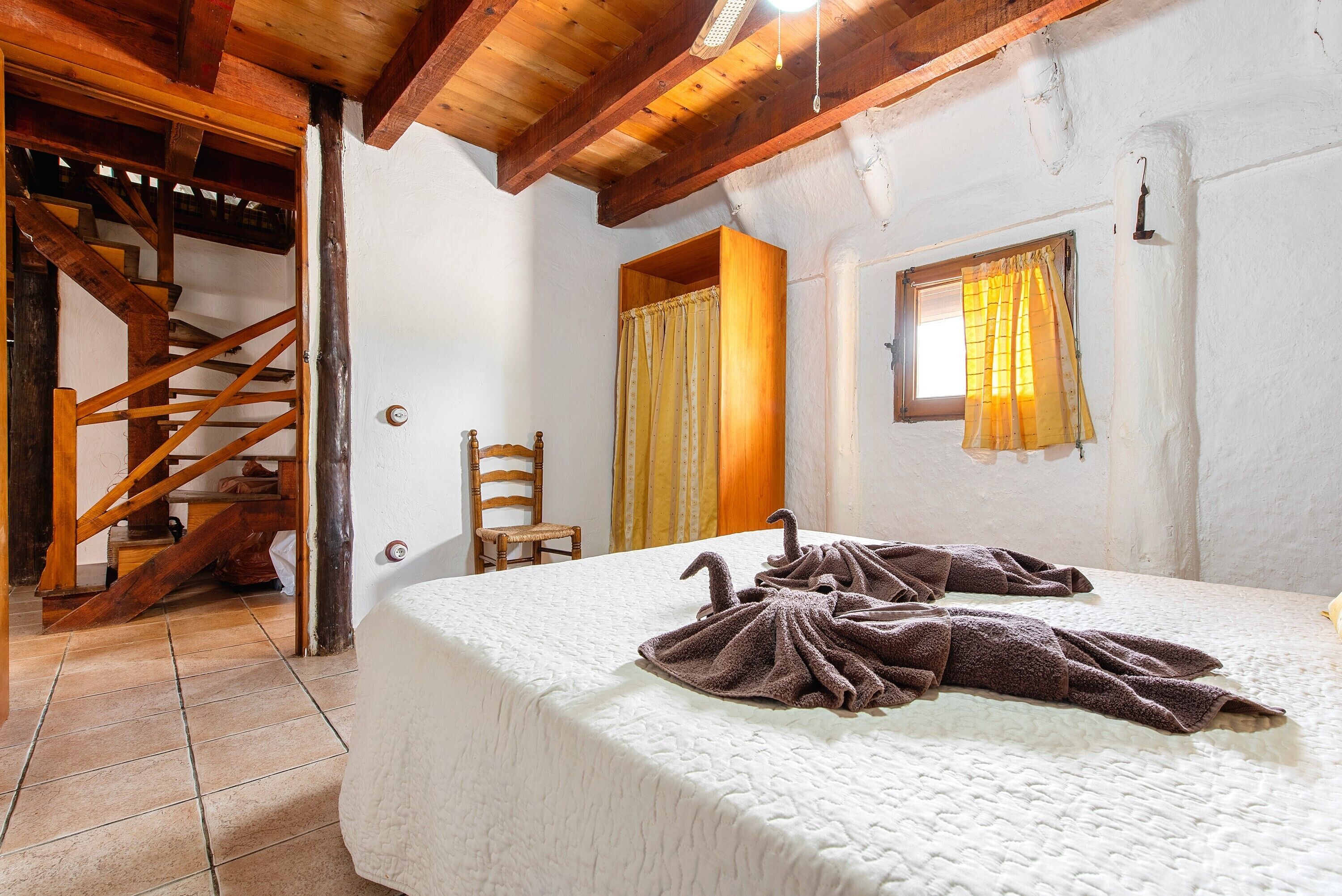 Una camera da letto con un letto, una scala in legno e una finestra con tende.