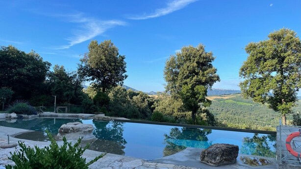Vista despejada de una piscina con solárium de piedra, rodeada de árboles y un paisaje montañoso.