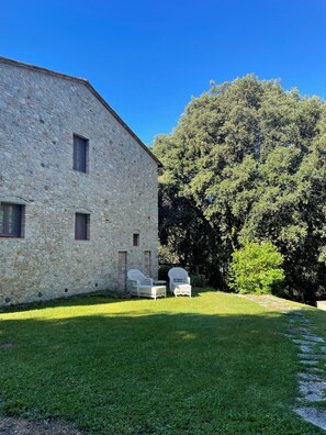 Un edificio in pietra con un cortile erboso e due sedie in vimini.