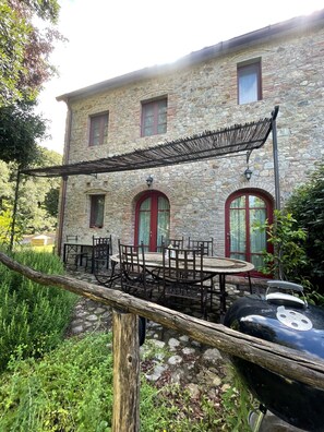 Un edificio in pietra con una zona salotto esterna coperta e un barbecue.