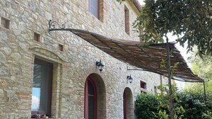 Un edificio de piedra con un patio cubierto, asientos exteriores y una pérgola.
