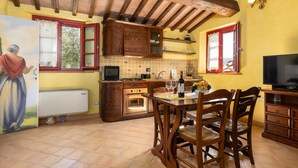 Een keuken met houten kastjes, een eettafel met stoelen, een televisie en een muurschildering.