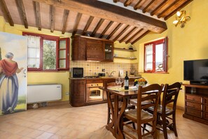 A kitchen with wooden cabinets, a dining table with chairs, a television, and a mural on the wall.