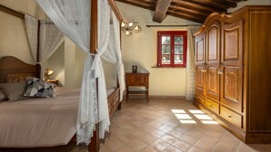 Een slaapkamer met een hemelbed, een houten garderobe en een raam met rode luiken.