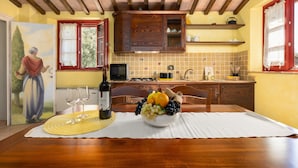 Een eethoek met een houten tafel, een schaal fruit, wijnglazen en een schilderij aan de muur.