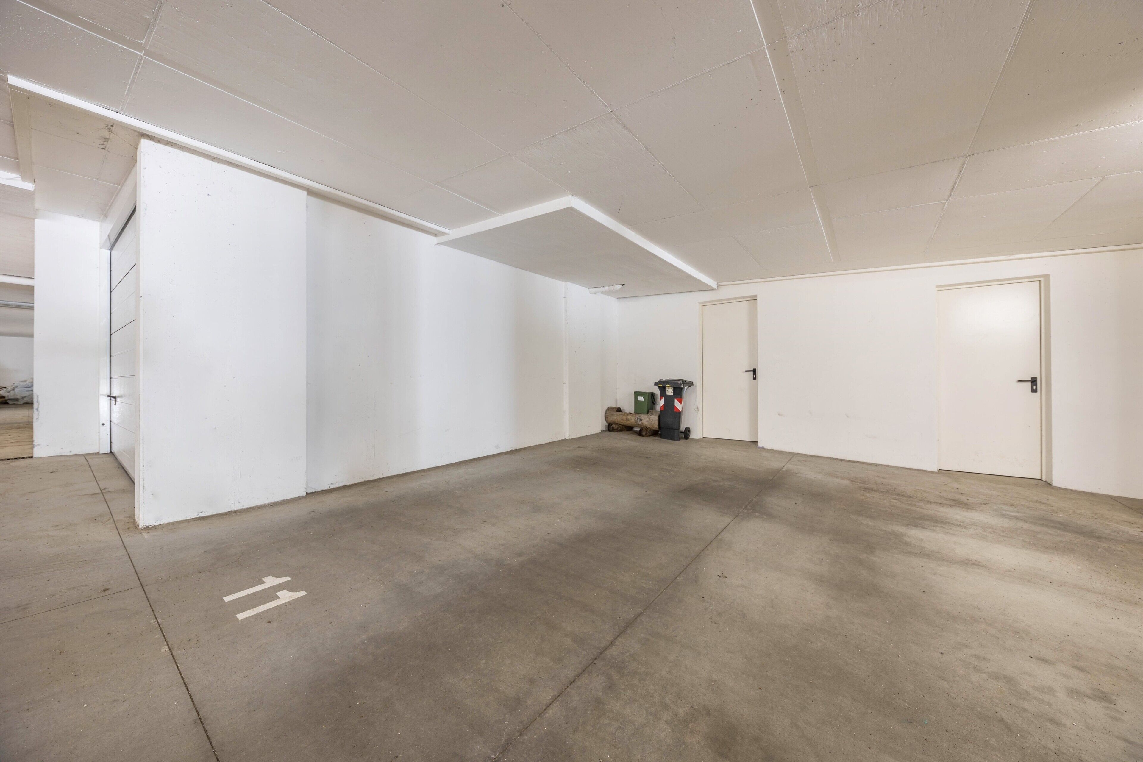 A spacious, empty room with white walls and a concrete floor, featuring a door and a small piece of equipment in the background.