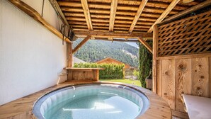 Een houten jacuzzi met uitzicht op een berg en een huis op de achtergrond.