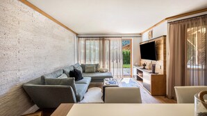 Een moderne woonkamer met een bank, salontafel, televisie en uitzicht door grote ramen.