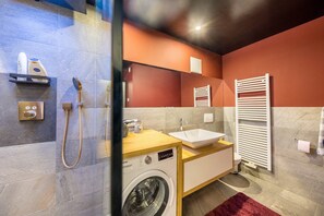 Uma casa de banho moderna com máquina de lavar, lavatório, porta-toalhas e chuveiro.