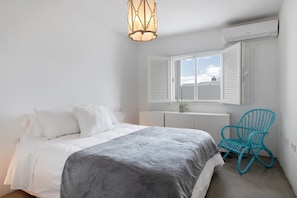 A bedroom with a bed, a chair, a window with shutters, and an air conditioning unit. - Vacation Home 'Casa La Concha Lanzarote' with Shared Pool, Private Terrace and Wi-Fi (Playa Honda)