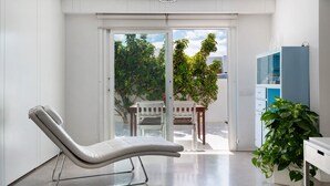 Habitación moderna con una butaca reclinable, un escritorio, una planta en maceta y vistas a un espacio exterior a través de un ventanal.