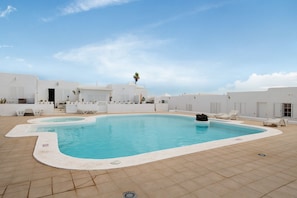 A rooftop swimming pool with white walls, a clear blue sky, and a palm tree. - Vacation Home 'Casa La Concha Lanzarote' with Shared Pool, Private Terrace and Wi-Fi (Playa Honda)