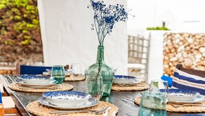 A dining table set with blue and white plates, a green glass bottle with flowers, and clear glasses. - Charming Holiday Home with Sea Views, Private Pool and Wi-Fi (Binibèquer)