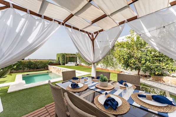 An outdoor patio with a pool, dining table set with placemats and napkins, and wicker furniture.