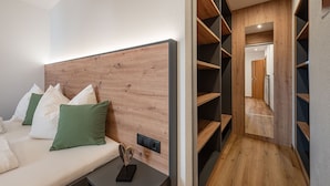 Una habitación de hotel moderna con cabecera de madera, cama con almohadas blancas y verdes, mesita de noche con un adorno y armario empotrado con estantes.