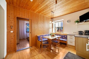 Una habitación con paneles de madera, una mesa de comedor, sillas, un banco, una zona de cocina y un televisor.