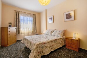 A bedroom with a bed, a nightstand, a dresser, a window with curtains, and a wall-mounted picture.