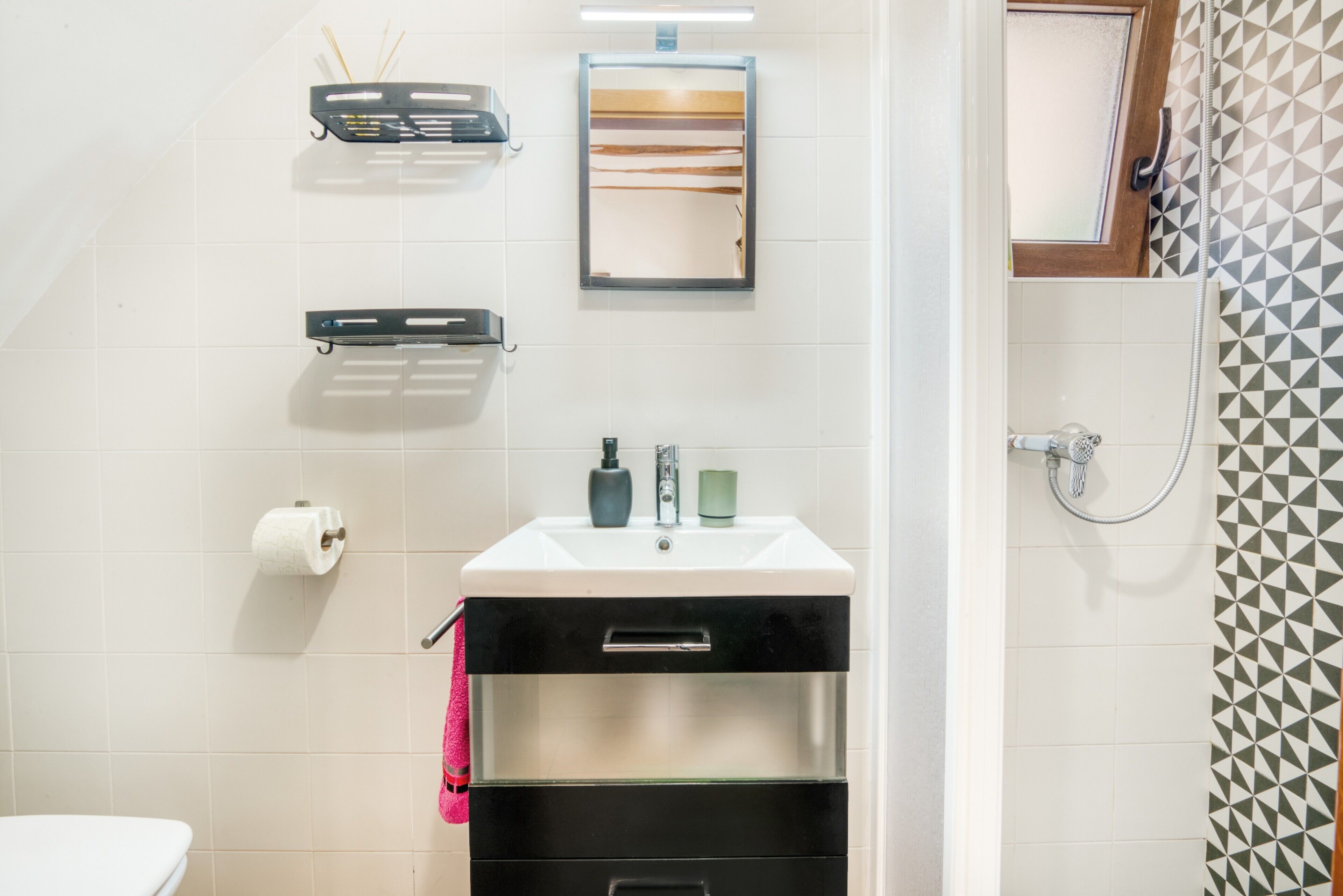Un baño con inodoro, lavamanos con espejo, toallero y zona de ducha.