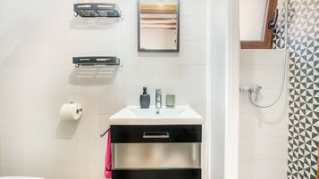 Un baño con inodoro, lavamanos con espejo, toallero y zona de ducha.