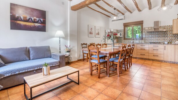 Een gezellige zithoek met een bank, een eettafel met stoelen, een salontafel en een keuken met kastjes en een raam.