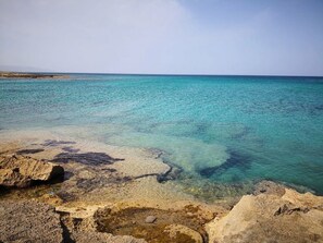 A coastal landscape with clear turquoise water, rocky formations, and a distant shoreline.