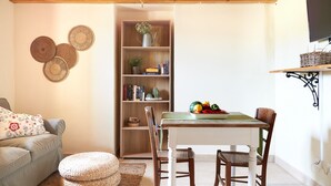 A cozy living room with a wooden ceiling, a bookshelf, a dining table with chairs, a TV mounted on the wall, and a decorative wall hanging. - Holiday Home 'Casa Degli Ulivi' with Private Terrace and Wi-Fi (Marzamemi)