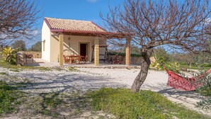 A small house with a tiled roof, a patio with chairs, and a hammock. - Holiday Home 'Casa Degli Ulivi' with Private Terrace and Wi-Fi (Marzamemi)