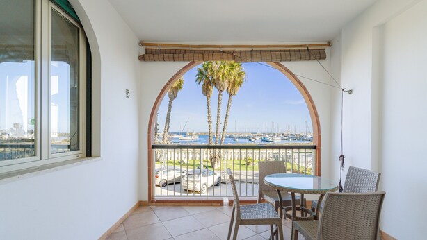 Un balcon donnant sur un port de plaisance, une table avec des chaises et un pot de fleurs.