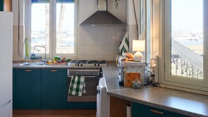 Une cuisine avec des armoires de couleur turquoise, une cuisinière à gaz, une hotte en acier inoxydable et une fenêtre donnant sur le port.