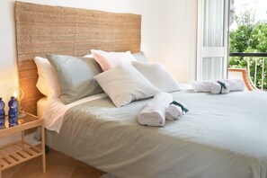Una cama bien hecha con almohadas, una mesita de noche con botellas de agua y vistas a zonas verdes a través de una ventana.