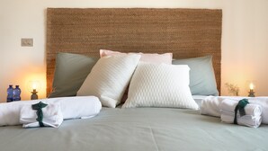 Un lit bien fait, avec une tête de lit en osier, des oreillers et des serviettes pliées.