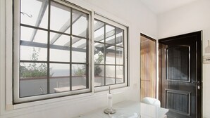 Ein Zimmer mit großem Fenster, einem weißen Tisch mit Glasplatte und einer schwarzen Tür.