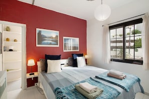 Un dormitorio con cama, mesitas de noche, una ventana con cortinas e imágenes colgadas en la pared.