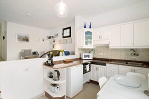 Cocina compacta con muebles blancos, microondas, cafetera y una mesa de comedor de vidrio.
