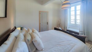 Un dormitorio con una cama grande, una ventana con cortinas, una puerta y una lámpara colgante.