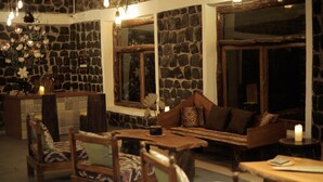 A cozy room with stone walls, wooden furniture, and a large window. - Bandhavgarh Meadows (Manpur)