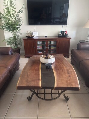 A living room with a wooden coffee table, leather sofas, a TV, and a cabinet with books.