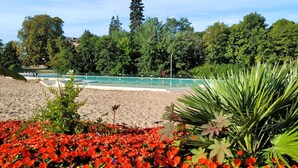Uma praia arenosa com piscina, rodeada por árvores verdes densas e flores vermelhas vibrantes.