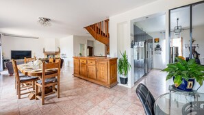 Uma sala de estar ampla com uma mesa e cadeiras de madeira para refeições, uma cozinha com eletrodomésticos modernos e uma escada que leva a um andar superior.
