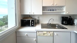 A modern kitchen with white cabinets, a microwave, a toaster, a sink, and a coffee maker. - 4-person apartment near the beach in Sables-d’Or-les-Pins | Ref 107 (FREHEL)