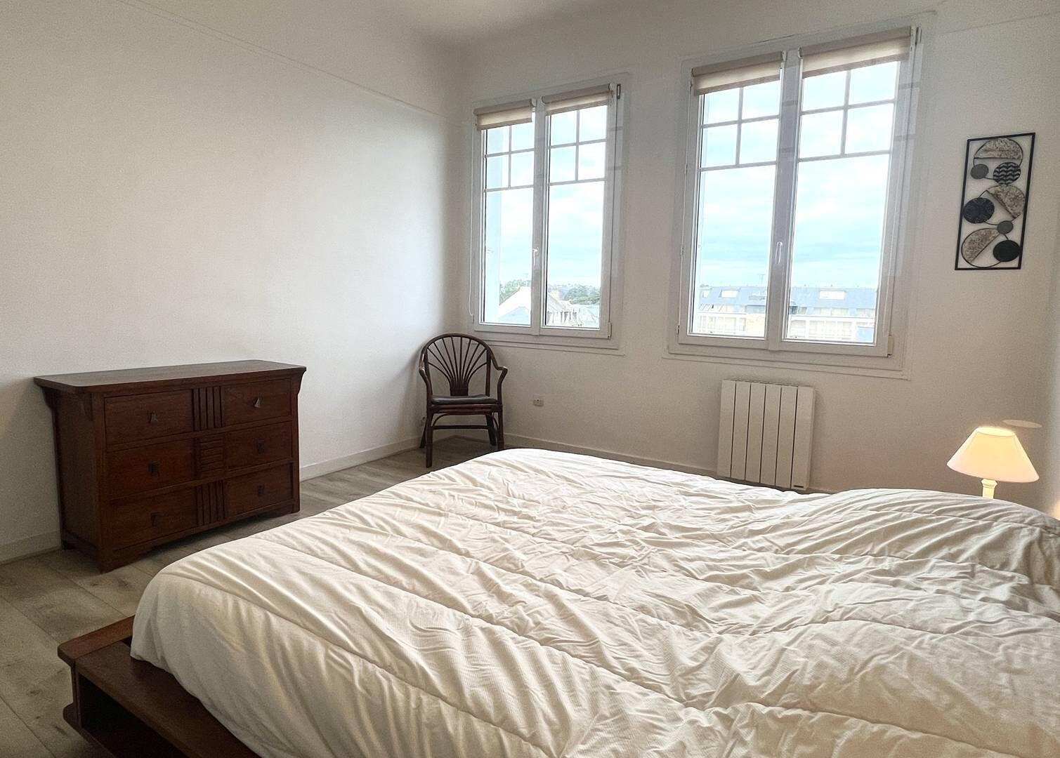 Une chambre à coucher avec un lit, une commode, une chaise et une fenêtre.