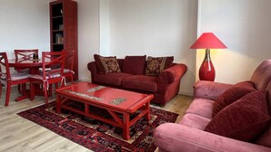 A living room with a red sofa set, a matching coffee table, a red lamp, and a bookshelf. - 4-person apartment near the beach in Sables-d’Or-les-Pins | Ref 107 (FREHEL)