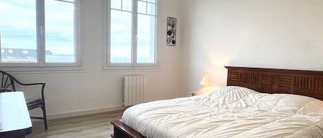 Een slaapkamer met een groot bed, twee ramen, een radiator en een bureau.