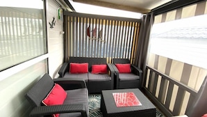A balcony with wicker furniture and red cushions, a view of the city, and a wooden ceiling. - Charming chalet located in a 4-star  campsite - 6 people (GUIDEL-PLAGES)